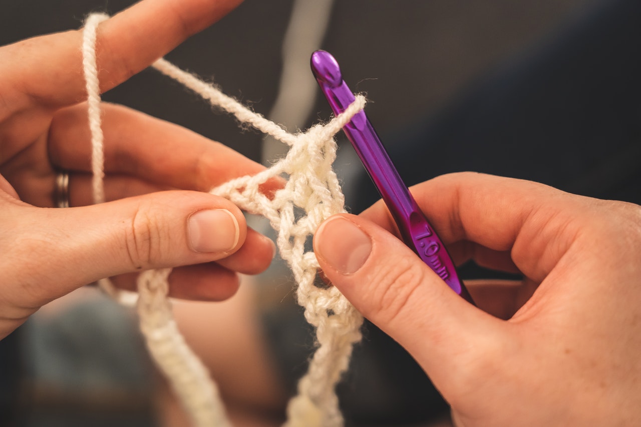 Person holding a purple crochet hook and white yarn